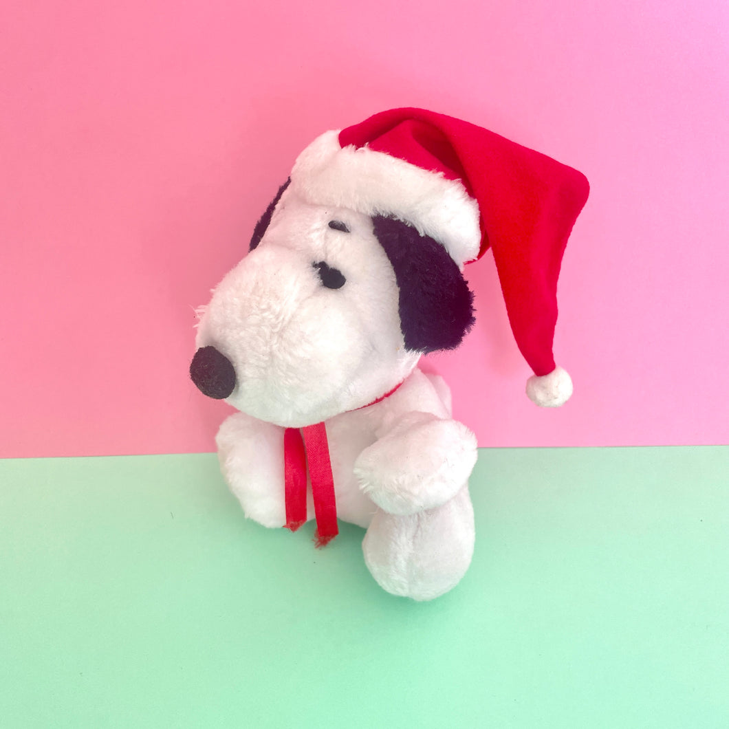 snoopy plush in a red Santa hat with white furry rim and white bobble not he end . wearing a red satin ribbon Around the neck 